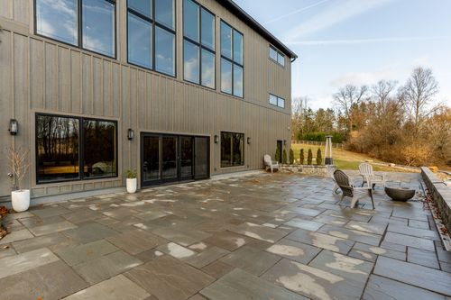 Stone patio with sliding glass doors, a patio heater and Adirondack chairs around a fire pit