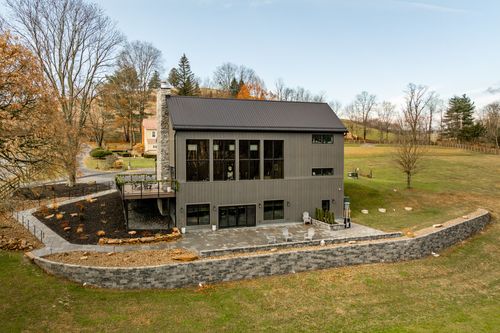 Aerial view of a modern barn-style venue with gray board-and-batten siding, stone chimney and curved stone patio wall