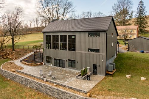 Aerial view of a barn-style venue with a metal roof, stone chimney and detached outbuilding amid rolling fields