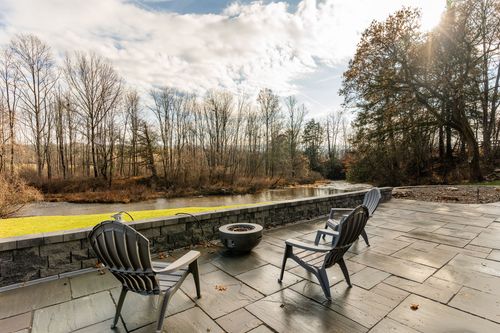 Fire pit patio with black Adirondack chairs overlooking a tree-lined creek at golden hour