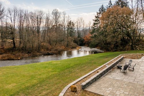 Grassy lawn leading down to a winding creek beside a stone-walled patio with fire pit seating
