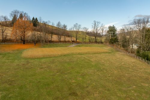 Aerial view of a manicured lawn ringed by split-rail fencing and a rolling autumn hillside