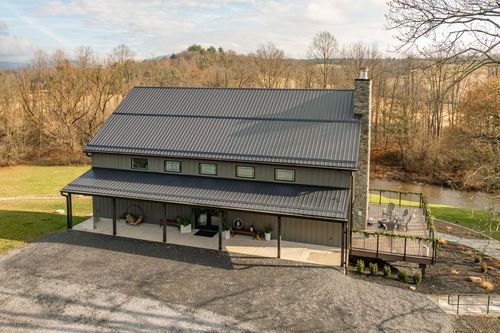 Aerial view of a barn-style venue with a stone chimney beside a wooded creek