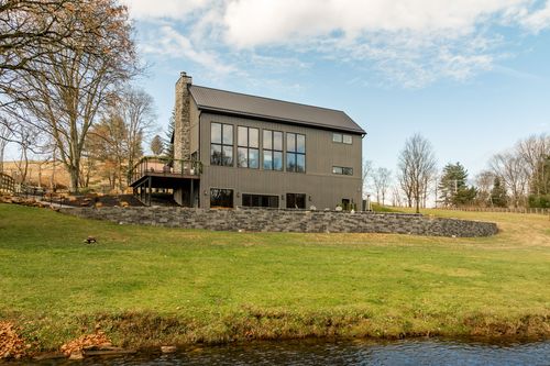 Exterior of the barn-style venue with a stone chimney and retaining wall overlooking a creek