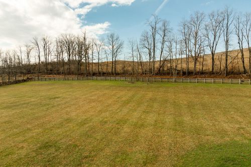 Aerial view of a fenced pasture with bare trees and rolling farmland in the distance