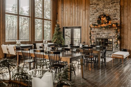 Wood-paneled dining hall with a stone fireplace, wreath and long tables set for a holiday gathering