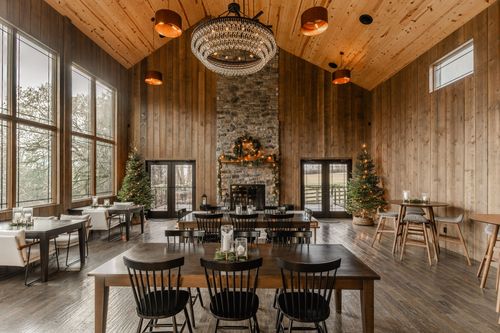 Great room with a vaulted pine ceiling, ornate chandelier and floor-to-ceiling windows overlooking the woods