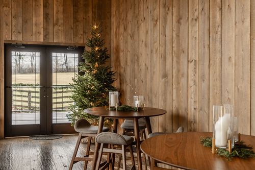 Wood-paneled dining nook with round cocktail tables and a lit Christmas tree by French doors