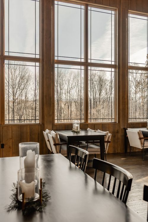 Window-side dining table with pillar candles and upholstered chairs overlooking bare trees
