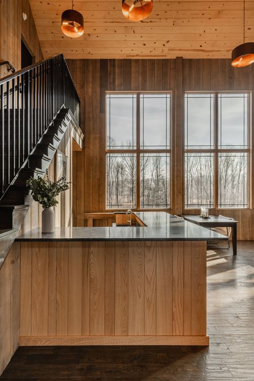 Wood-paneled kitchenette with a dark stone countertop and black staircase railing