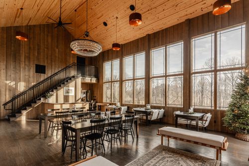 Open event room with a loft staircase, bar area and long tables beneath a vaulted pine ceiling