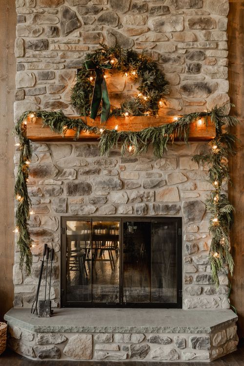 Stacked stone fireplace decorated with a pine wreath, string lights and garland