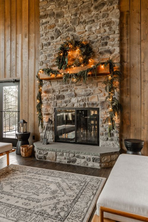 Stone fireplace with holiday garland flanked by upholstered benches and a patterned rug