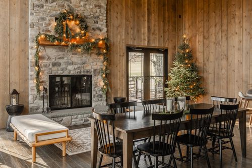 Dining area beside a garland-draped stone fireplace with a lit Christmas tree