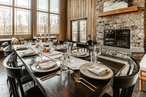 Dining table set beside a stone fireplace with framed artwork and lit taper candles