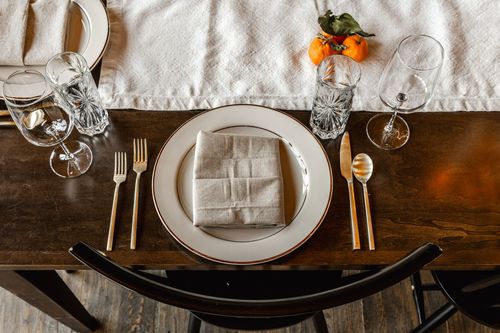 Overhead view of a table setting with a gold-rimmed plate, linen napkin and clementines