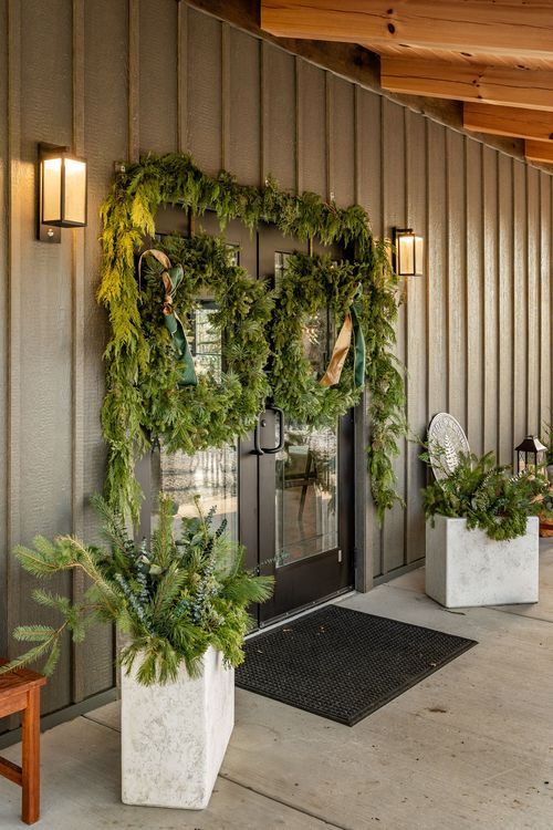 Double entry doors decorated with pine garland and wreaths, flanked by wall sconces