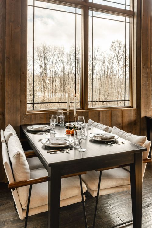 Window banquette seating with cream cushions set for a meal overlooking bare trees