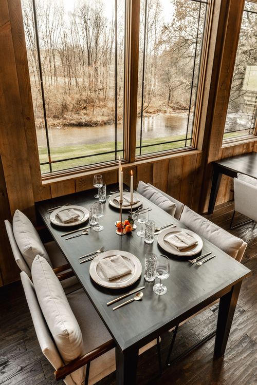 Upholstered banquette table set beside windows overlooking a winding creek