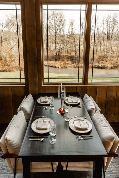 Window-side banquette table set with lit candles and a wooded creek view beyond