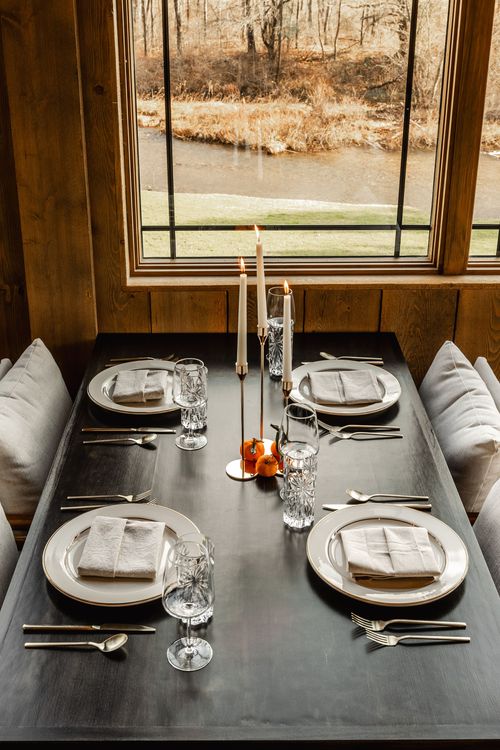 Dining nook with cushioned bench seating overlooking a creek through tall windows