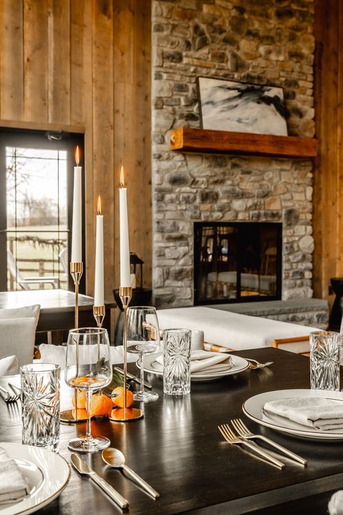 Place setting with lit taper candles in front of a stacked stone fireplace