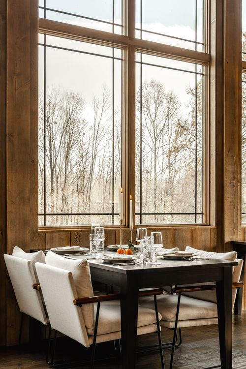Corner banquette table set with white upholstered chairs beneath large windows