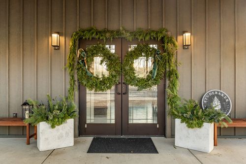 Double entry doors dressed with pine wreaths and garland, flanked by wood benches