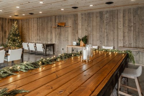 Long wood communal table strung with garland lights beside a decorated Christmas tree