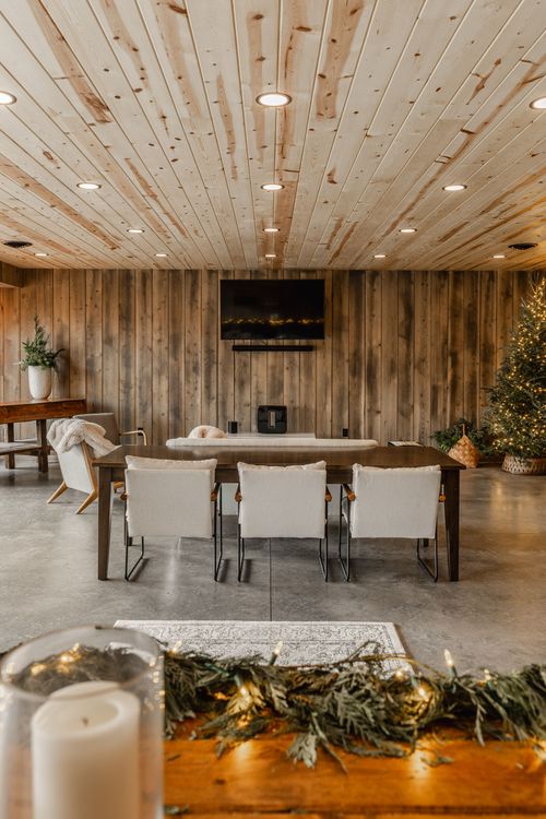Wood-paneled lounge with a dining table set for six, TV and pine wreath accents