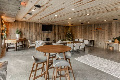 Casual seating area with a round bistro table, wooden stools and a mounted television