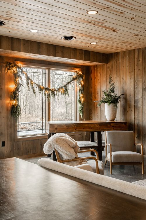 Window nook wrapped in lit garland with an armchair, sherpa throw and potted greenery