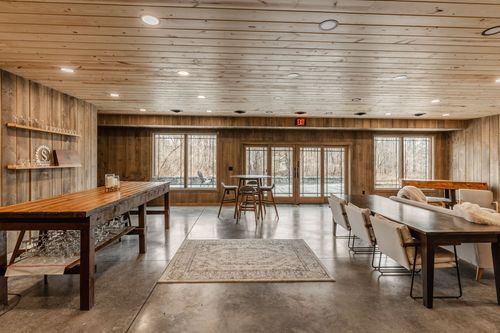 Multi-purpose room with high-top tables, wood bench seating and windows overlooking the woods