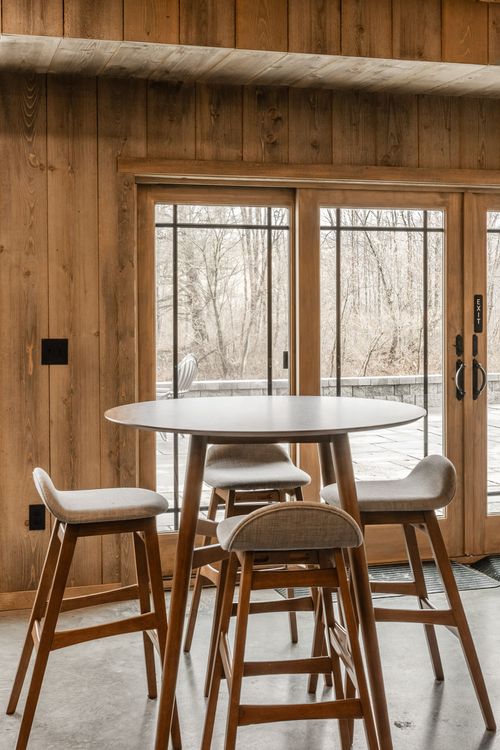 Round pub table with four wooden stools set beside glass doors to the patio