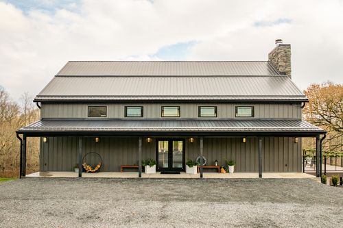 Front exterior of a barn-style venue with a metal roof and covered gravel-lot entrance