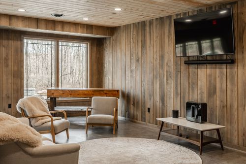 Corner sitting area with upholstered chairs, a wood bench and a mounted TV