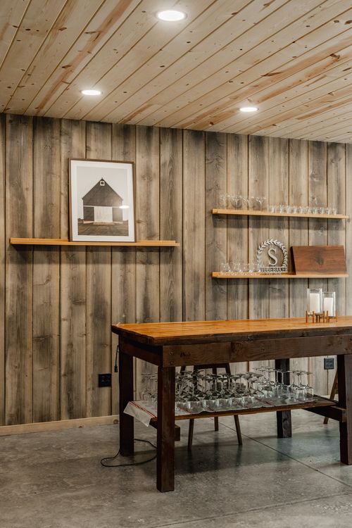 Rustic wood table beneath shelving with glassware and a framed barn print