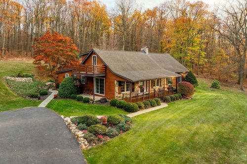 Aerial view of a log-style ranch home surrounded by vivid fall foliage and a curved driveway