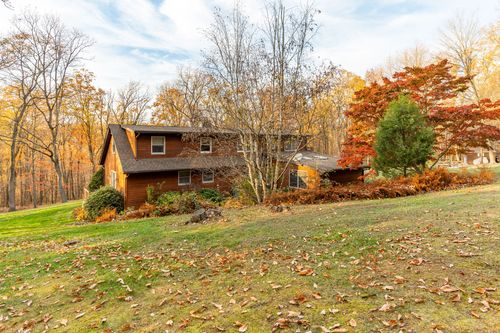 Side exterior of a log-sided home tucked into a wooded autumn lot