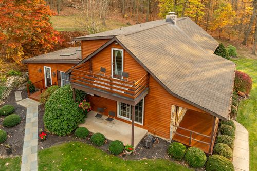 Aerial view of a log home's shingled roof and second-story deck surrounded by fall trees