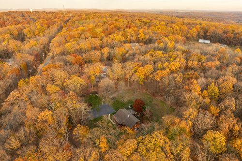 Aerial view of a forested lot with a long gravel driveway winding through fall foliage