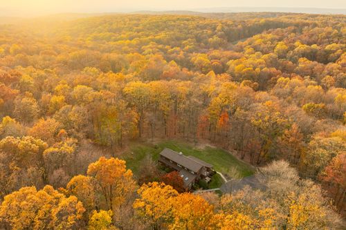 Aerial view of a home in a small forest clearing surrounded by autumn color