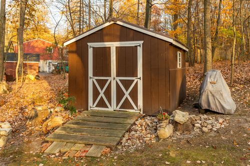 Wood storage shed with white trim doors set among fall trees