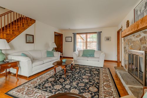 Living room with a wood staircase, white sofas and a stone fireplace