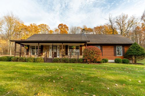 Front exterior of a log-sided ranch home with a covered wraparound porch and manicured lawn