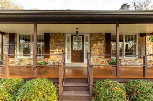 Covered front porch with stone columns, wood flooring and a paneled entry door