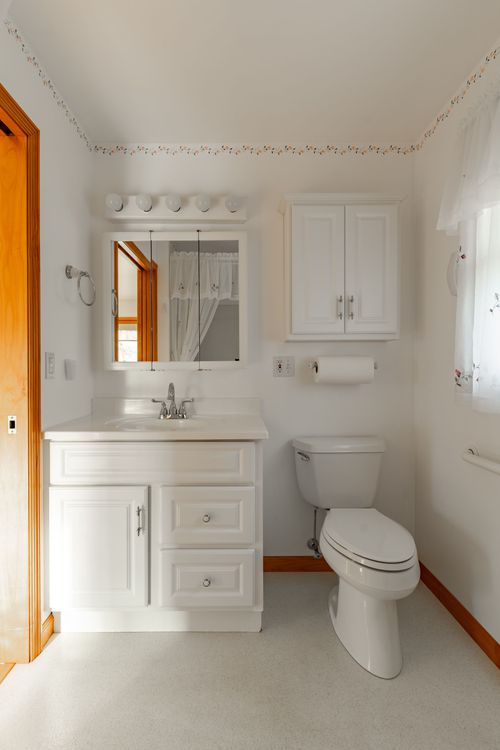 Bathroom with white fixtures, a floral wallpaper border and wood-trimmed mirror