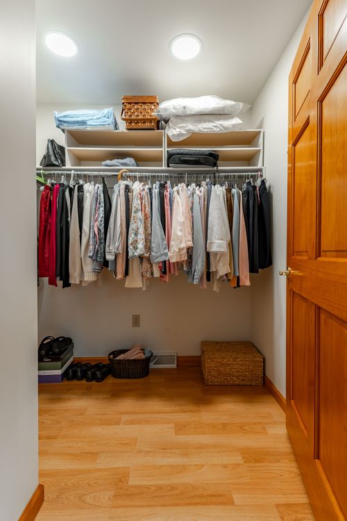 Walk-in closet with hanging clothes, built-in shelving and a wood paneled door