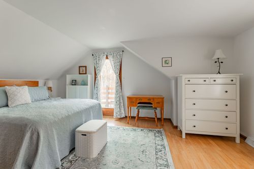 Bedroom with floral curtains, a white dresser and wood paneled closet doors