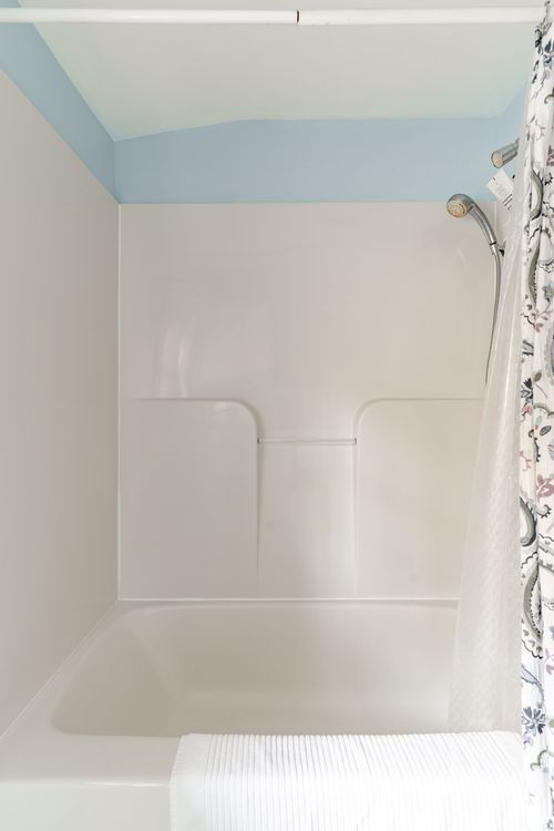 Bathtub and shower combo with a floral curtain and light blue ceiling